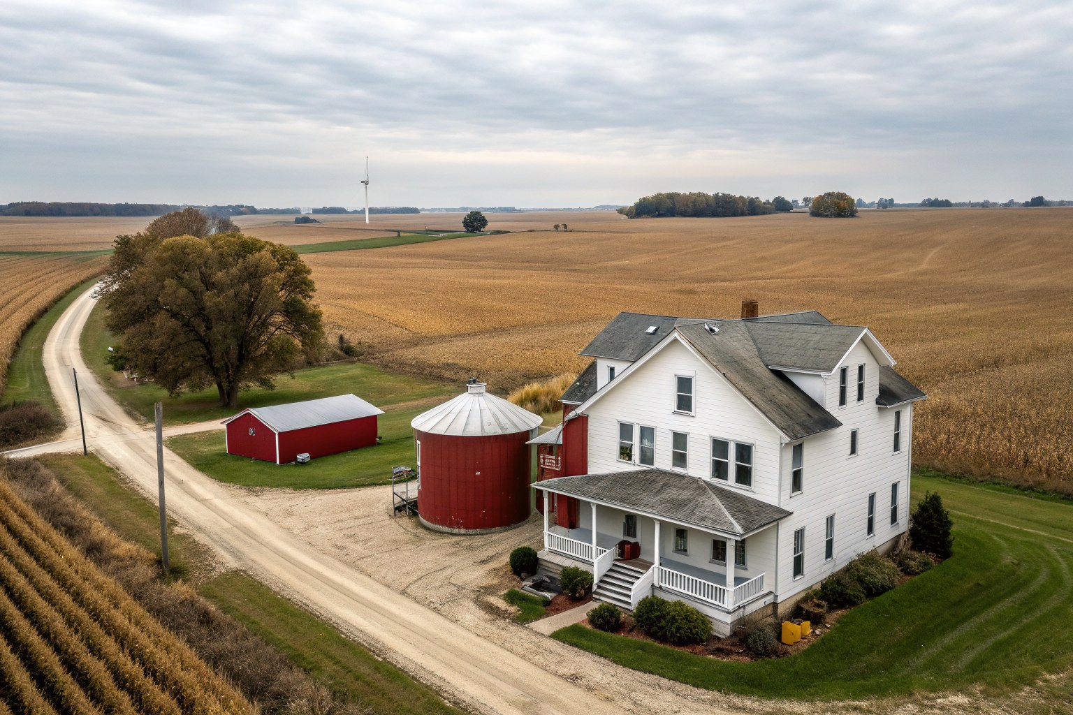 White farmhouse with a red barn and grain bins beside flat harvested fields