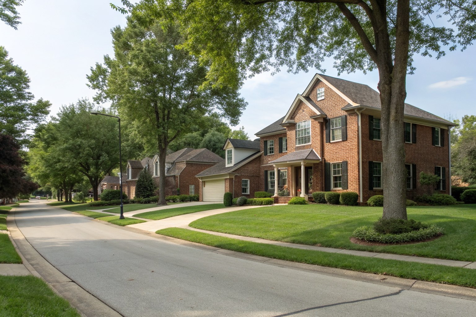 Two-story home with a brick front on a curving street lined with trees